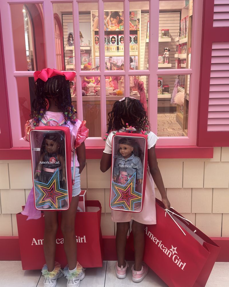 The sisters wearing doll-carrier backpacks, looking into a toy store window