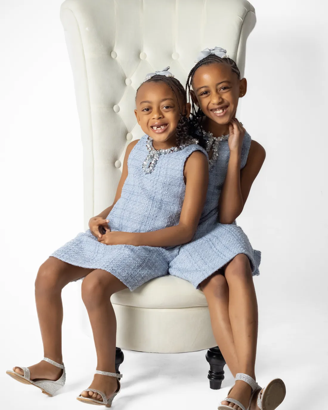 Mila G and Mati K smiling in matching blue dresses on a white chair